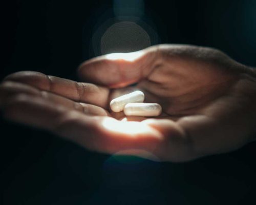 Hand holding 2 pills in sunlight.